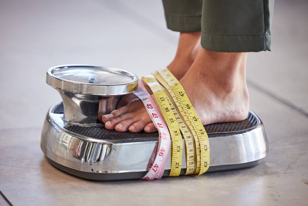 Δίαιτα, απώλεια βάρους και τα πόδια μιας γυναίκας σε μια κλίμακα για τον έλεγχο του σώματος, τη μέτρηση και την ισορροπία για να χάσουν βάρος στο πάτωμα. Η παχυσαρκία, κλίμακες και το κορίτσι με μέτρο ταινία για εμμονή με την υγεία και την εικόνα του σώματος. - Φωτογραφία, εικόνα