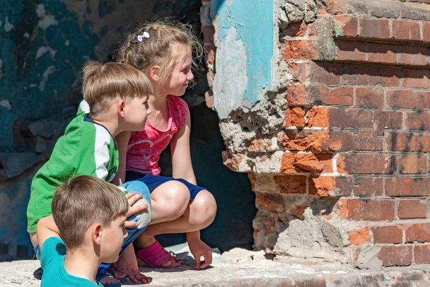 Drei Kinder in einem zerstörten Haus verstecken sich vor militärischen Konflikten, Flüchtlingskinder leiden unter der Zerstörung terroristischer Gewaltakte. Einreichungsfoto. - Foto, Bild