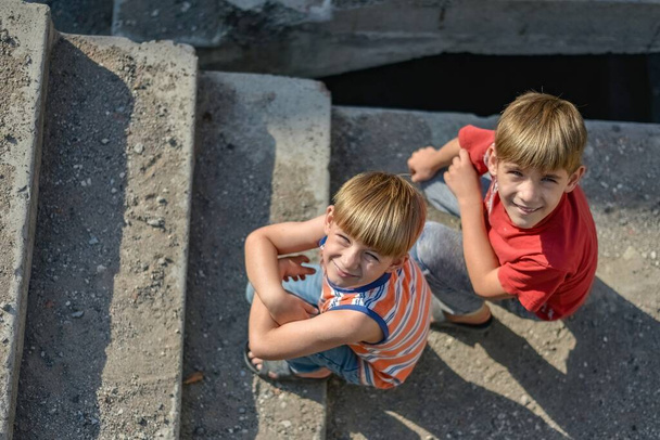 Dwoje dzieci siedzi na schodach opuszczonego budynku, koncepcja życia sierot dzieci ulicy. - Zdjęcie, obraz