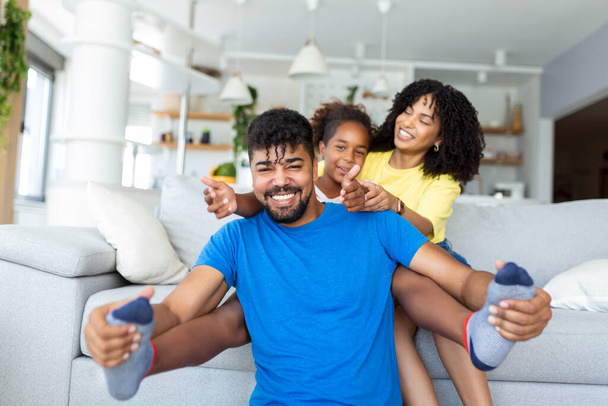 Ευτυχισμένος Αφρο-Αμερικανός μπαμπάς και μαμά με ενθουσιασμένο περήφανο παιδί κόρη, που παίζει τον ιπτάμενο υπερήρωα, που απλώνει χέρι μπροστά. Χαρούμενο κορίτσι που παίζει ενεργό παιχνίδι με την οικογένεια στο σπίτι - Φωτογραφία, εικόνα