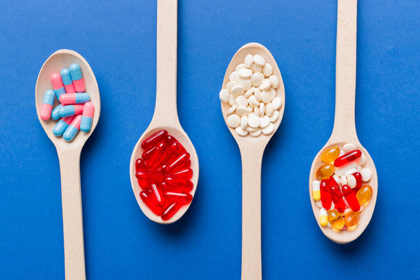 Vitamin capsules in a spoon on a colored background. Pills served as a healthy meal. Red soft gel vitamin supplement capsules on spoon. - Valokuva, kuva