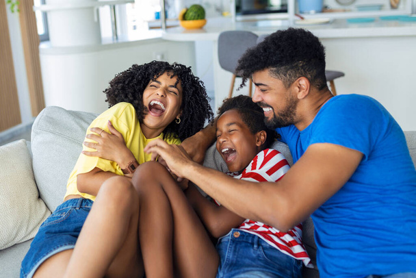 Cheerful people sitting on couch in living room have fun little daughter tickling mother laughing together with parents enjoy free time playing at home. Weekend activity happy family lifestyle concept - Photo, Image