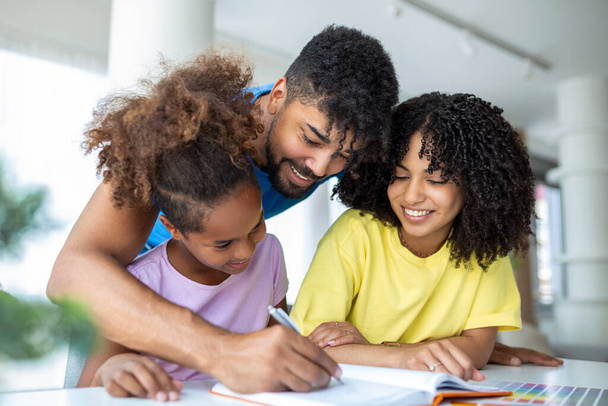 Vista frontale dei genitori afroamericani che aiutano la figlia con i compiti a tavola, - Foto, immagini