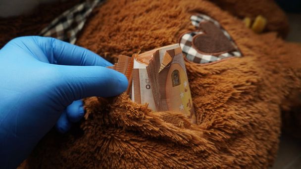 uma mão enluvada recupera dinheiro de um cache encontrado em um brinquedo macio   - Foto, Imagem