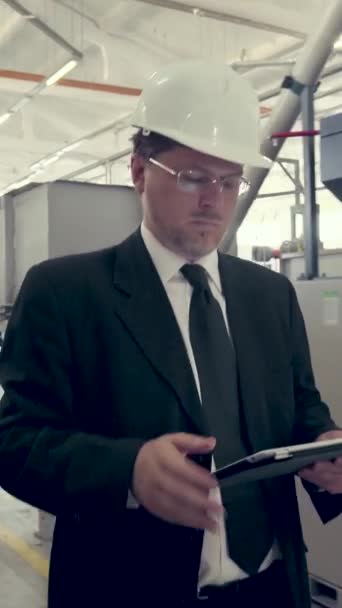 Liikemies kävelee tehtaan läpi tabletin kanssa. Pystysuora video - Materiaali, video