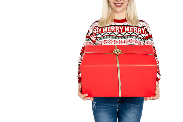 Неузнаваемая женщина держит рождественский подарок. Неузнаваемая женщина продвигает продажи подарком, одетым в рождественский свитер и в шляпу Санта Клауса. Студийный фон белый - Фото, изображение