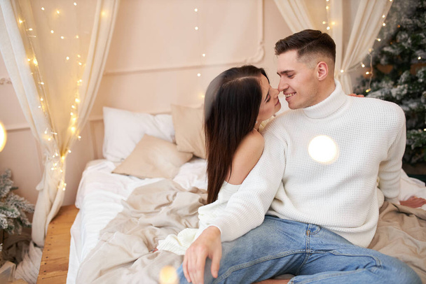 Tutkulu romantik çift yeni yıldan önce evde çelenklerle vakit geçiriyor. Seksi genç bir kadın ve yatakta kazak giyip sarılan yakışıklı bir adam. Birlikte şefkatli bir çift - Fotoğraf, Görsel
