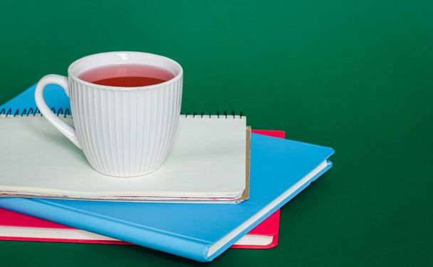 Notizbücher und eine Tasse Tee auf grünem Hintergrund, das Konzept von Arbeit und Studium, Kopierraum. - Foto, Bild