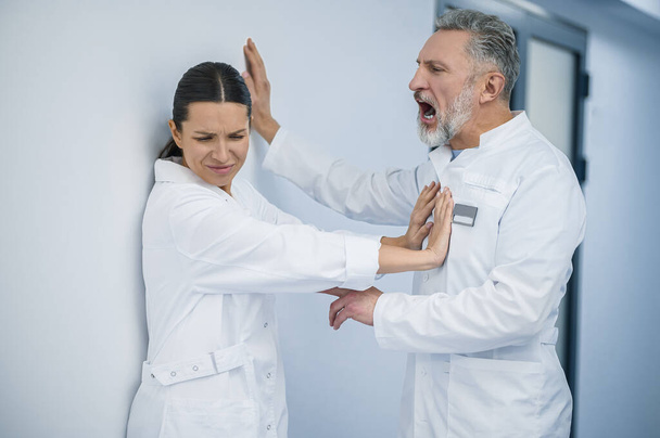 Seksuaalista häirintää. Naislääkäri torjuu flirttaileva käyttäytyminen hänen miespuolinen kollegansa - Valokuva, kuva