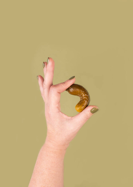 Eine Frauenhand hält eine Essiggurke und zeigt eine OK-Geste. Konzept des Urlaubs Shape Up With Pickles Time. Vertikaler Schuss - Foto, Bild
