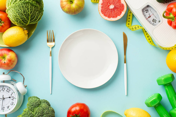 Concept nutritionnel approprié. Top vue photo de plaque couteau fourchette échelles légumes fruits réveil haltères et ruban à mesurer sur fond bleu pastel isolé avec espace vide - Photo, image