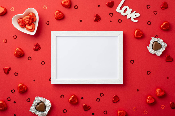 Η ιδέα του Αγίου Βαλεντίνου. Κορυφή φωτογραφία άποψη του λευκού κορνίζα σχήμα καρδιάς σοκολάτα καραμέλες δίσκο επιγραφή αγάπη και κομφετί σε απομονωμένο κόκκινο φόντο με κενό χώρο - Φωτογραφία, εικόνα