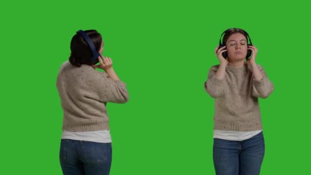 Close-up van de lachende vrouw die online naar muziek luistert, met behulp van een koptelefoon om van nummers op de radio te genieten. Jonge volwassene staan over greenscreen achtergrond en plezier hebben met mp3 geluiden, draadloze headset. - Video