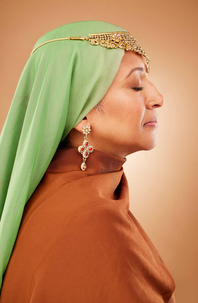 Muzułmanin, ubrania kultury i starsza kobieta z biżuterią, wiarą i hidżabem na brązowym tle studio. Moda islamska, tradycyjny i skromny model burka z religią, duchem i szalikiem. - Zdjęcie, obraz
