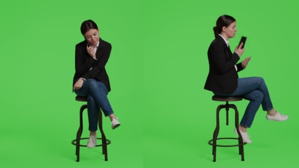 Caucasian businesswoman answering call on smartphone, sitting on chair in studio background. Office worker talking on remote telephone line using mobile phone, full body green screen backdrop. - Footage, Video