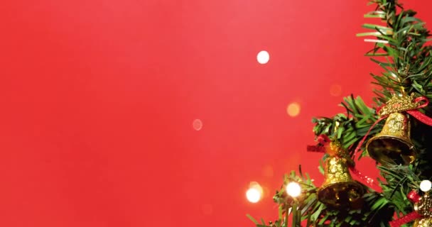 Kerstboom versierd met gouden klokken met bokeh lichten op rode achtergrond. - Video