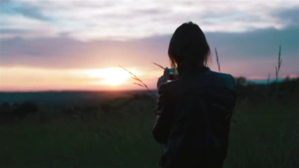 Young woman takes pictures of sunset with smartphone. Long shot and close-up - Footage, Video