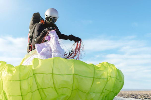 Man on professional suit and helmet taking his paraglider on a beautiful sunny day. Copy space on right side - Photo, Image