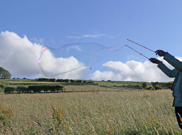 Riesenseifenblase mit Seifenblasenstab im Sommer auf einem Feld - Foto, Bild