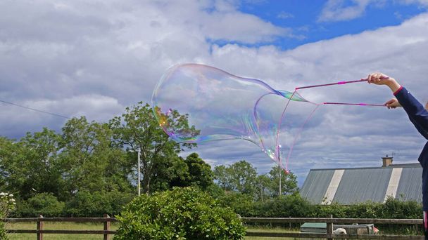Riesige Seifenblase mit einem Blasenstab im Garten - Foto, Bild