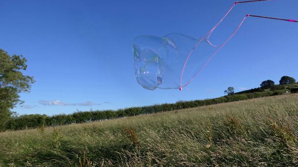 夏に畑にバブルワンドを持つ巨大ソープバブル - 写真・画像