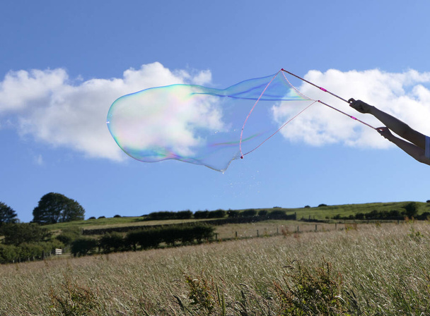 Óriási szappanbuborék egy buborékpálcával egy mezőn nyáron. - Fotó, kép