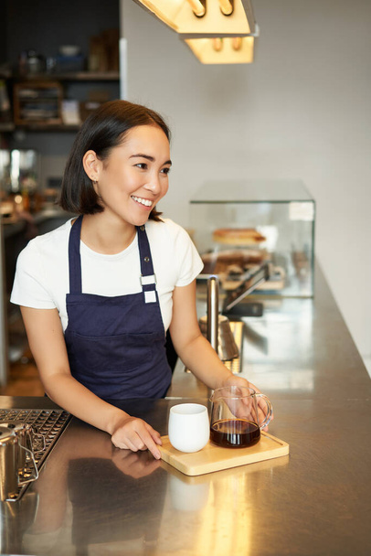 Vertikální záběr usměvavé asijské baristky, dívka pracující v kavárně, objednávka klientovi, dávkové vaření, filtrační káva. - Fotografie, Obrázek