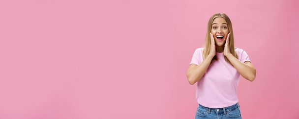 Verrukt en verbaasd vrolijke vriendin in t-shirt en jeans brede glimlach met geopende mond geamuseerd ontroerende wangen verrast en tevreden reageren op positieve verrassing over roze achtergrond. Begrepen. - Foto, afbeelding