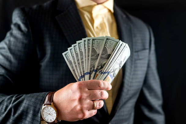 hombre de negocios con camisa y chaqueta cuenta billetes de cien dólares delante de su pecho. Concepto de dinero y comercio. De cerca. - Foto, imagen