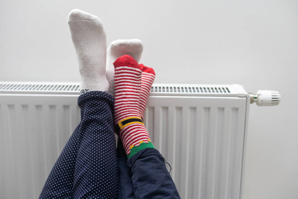 Moeder en kind verwarmende voeten in de buurt van verwarming thuis, close-up. - Foto, afbeelding