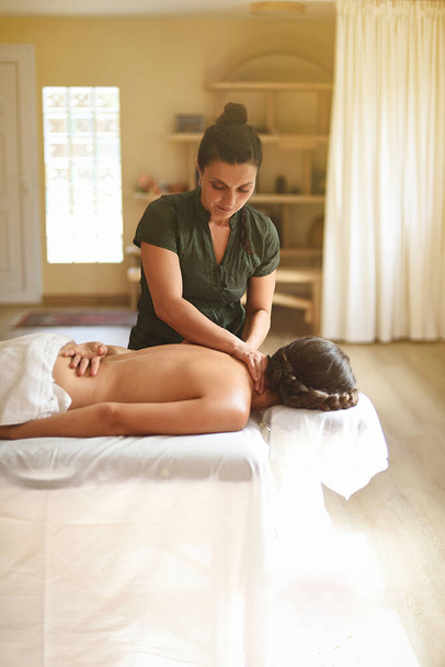 Kobieta w pracy robi masaż na stole do masażu w pokoju do masażu z ciepłym światłem. - Zdjęcie, obraz
