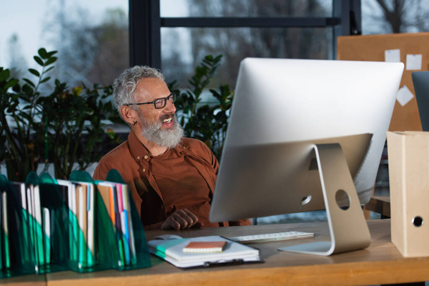 Pozitív középkorú üzletember néz távol számítógép és papírok irodai  - Fotó, kép