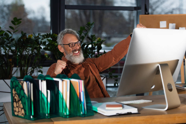 Izgatott ősz hajú üzletember mutatja igen gesztus közelében számítógép és a papírmunka az irodában  - Fotó, kép