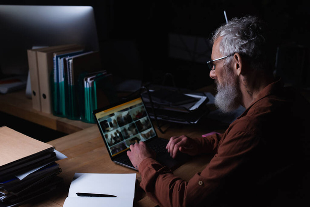 kypsä liikemies työskentelee kannettavan tietokoneen lähellä tyhjä muistikirja yöllä toimistossa - Valokuva, kuva