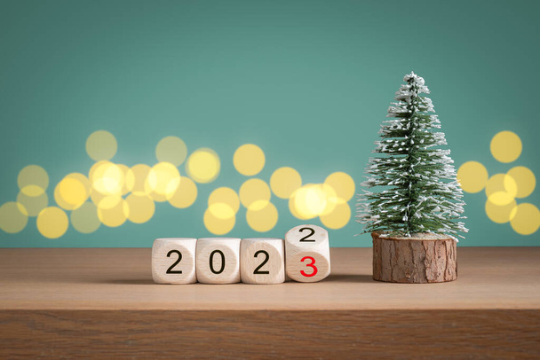 緑の背景の前で2023に変わる2022年の年番号を持つミニクリスマスツリーと木製のブロック。新年のコンセプト. - 写真・画像