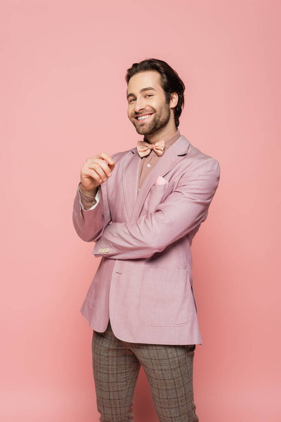 Smiling host of event in jacket and bow tie looking at camera on pink background  - Фото, зображення