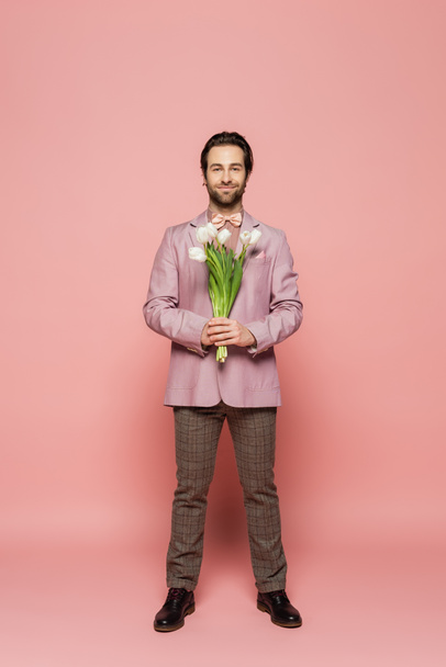 Full length of stylish host of event holding bouquet of tulips on pink background  - Foto, afbeelding