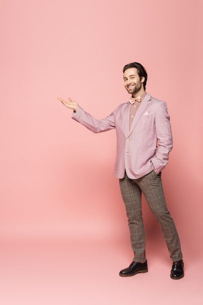 Full length of positive host of event pointing with hand on pink background  - Foto, imagen