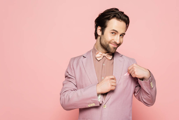 Smiling host of event in jacket touching handkerchief isolated on pink  - Photo, Image