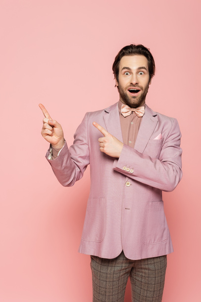 Lenyűgözött házigazdája esemény mutató ujjaival rózsaszín háttér  - Fotó, kép