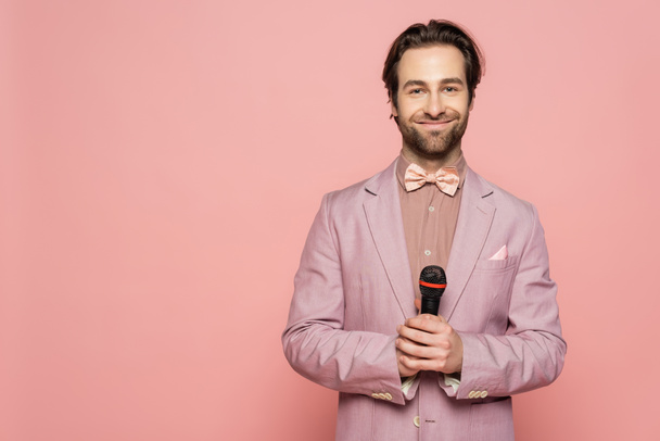 Young host of event holding microphone and looking at camera isolated on pink  - Foto, Bild