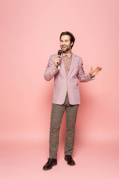 Full length of stylish host of event holding microphone on pink background  - Foto, imagen