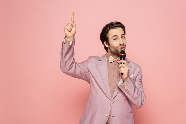 Young and stylish host of event holding microphone while having idea isolated on pink  - Фото, зображення