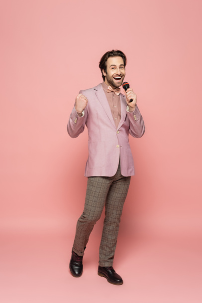 Full length of trendy host of event showing yes gesture and holding microphone on pink background  - Zdjęcie, obraz