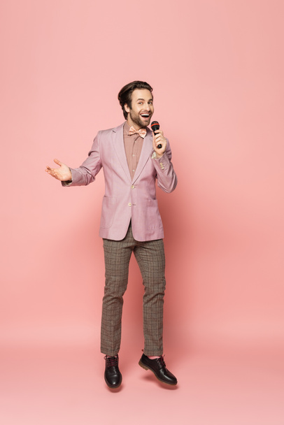 Pełna długość modnego gospodarza imprezy z mikrofonem podczas skakania na różowym tle  - Zdjęcie, obraz