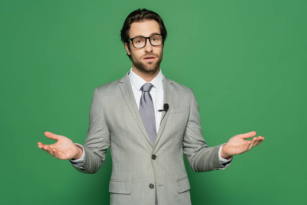 Newscaster in eyeglasses and clip microphone talking on green background  - Photo, Image