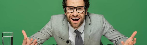 Emotionaler Nachrichtenanker in Brille und Anzug gestikuliert isoliert auf grünem Banner  - Foto, Bild