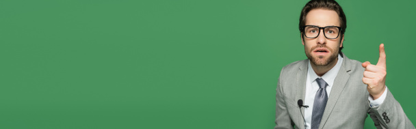 Эмоциональный ведущий новостей в очках и костюмах, указывающий пальцем на зеленый, баннер  - Фото, изображение