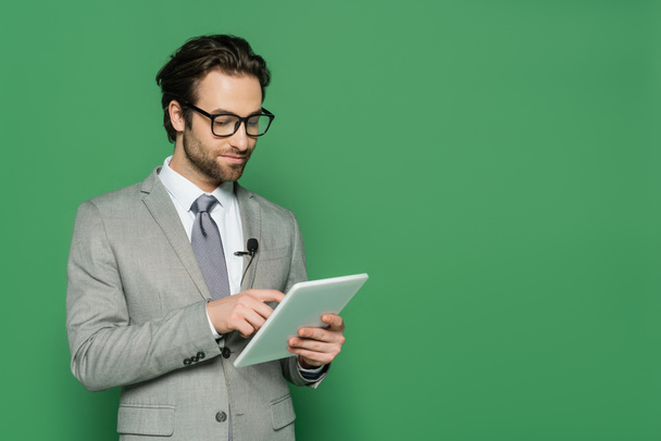 journaliste en lunettes et costume à l'aide d'une tablette numérique isolée sur vert  - Photo, image
