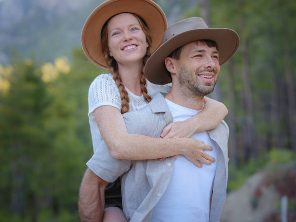 若い興奮したカップル2人の友人家族の男性の女性がカジュアルな服のボーイフレンドは喜びのガールフレンドに戻って夏の日に座ってピギーバックに乗るを与える。トルコに山の森の散歩 - 写真・画像